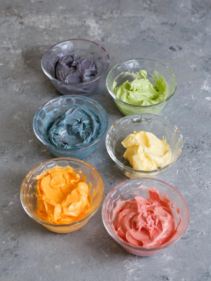 Six small bowls with colored buttercream frosting